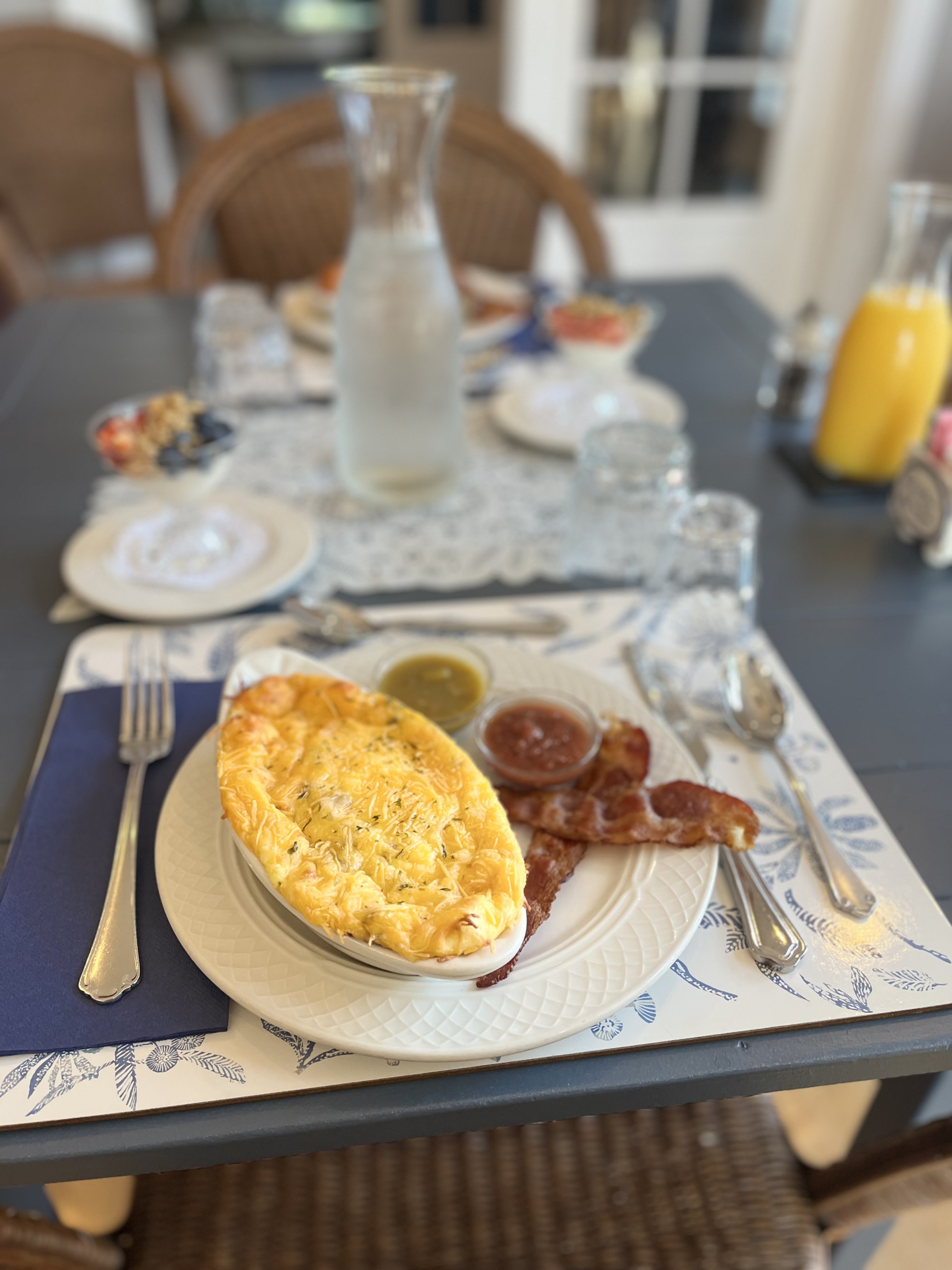 A breakfast plate with an omelette, bacon, and sauce on a table.