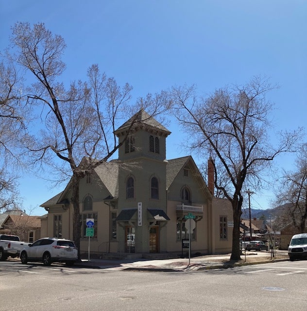 a tan building with a tower and a brown roof is on a street corner with cars parked in front of it