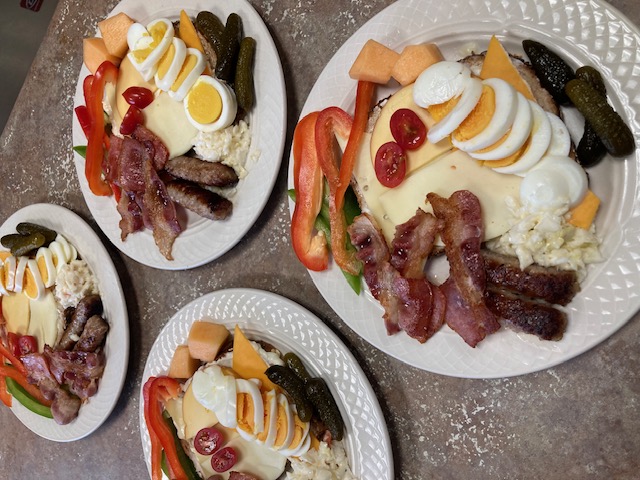 Four plates of breakfast food with eggs, bacon, peppers, and tomatoes
