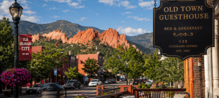 Old Colorado City street scene with a large black sign for Old Town Guesthouse and red rock formations in the background.