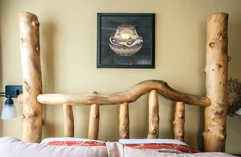 Close up view of bed with custom headboard made out of wooden logs