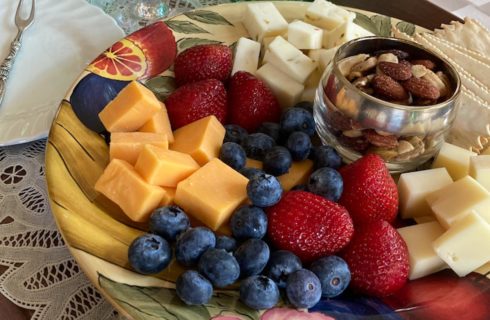 Close up view of plate full of multiple cheeses, strawberries, blueberries, crackers, and nuts