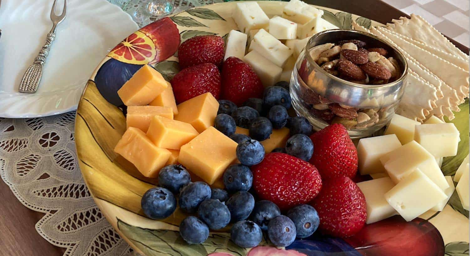 Close up view of plate full of multiple cheeses, strawberries, blueberries, crackers, and nuts