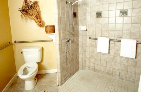 Bathroom with yellow walls, tiled flooring, grab bars by toilet, and walkin tiled shower