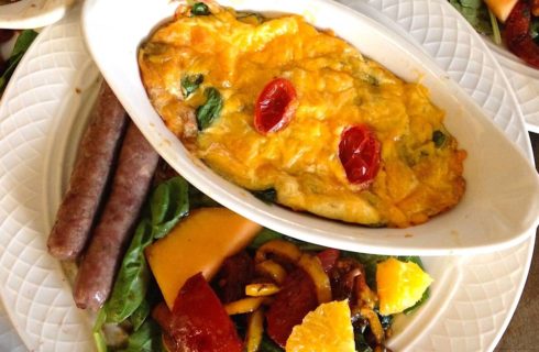 Close up view of a breakfast egg souffle, salad topped with fruit, and sausage links