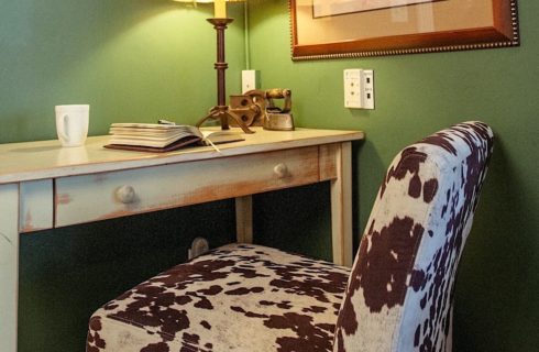 Close up view of antiqued white wooden desk with cow hide upolstered chair