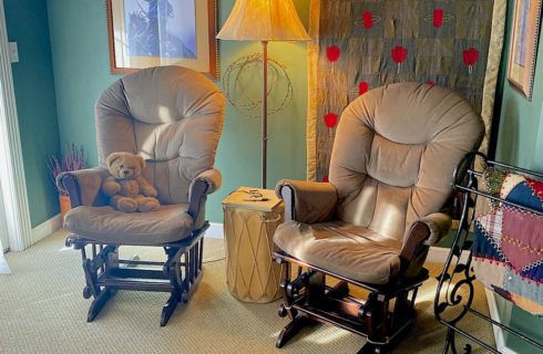 Sitting area with two taupe gliding rocking chairs, Native American drum, and floor lamp