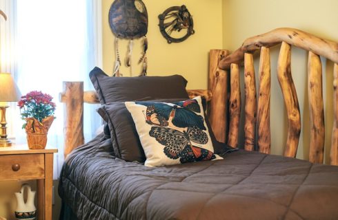 Small room with yellow walls, bed with log rails, brown bedding, and wooden nightstand