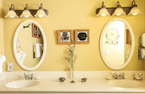 Bathroom with yellow walls, double sink vanity, large counter, and two oval mirrors