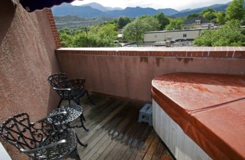 Balcony patio with covered corner hot tub, wrought iron chairs and small table, and view of the mountains in the background