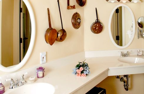 Bathroom with cream walls, double sinks, large counter, two oval mirrors, and a mini-fridge