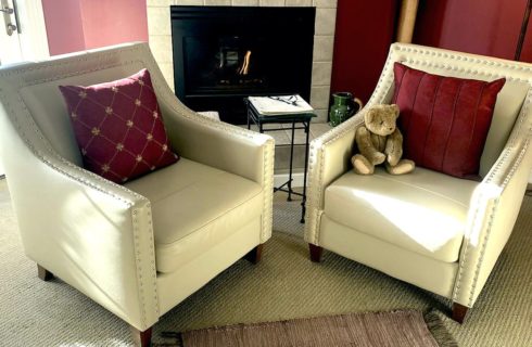 Sitting area with two white leather armchairs, small table, and fireplace