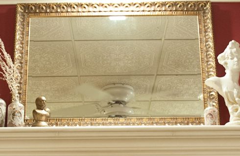 Close up view of white fireplace mantel, large ornate mirror, antique bottles, and marble female bust