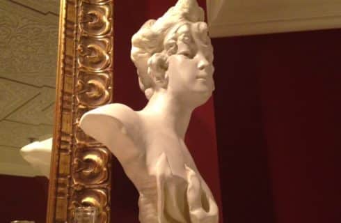 Close up view of a marble female bust next to large ornate mirror