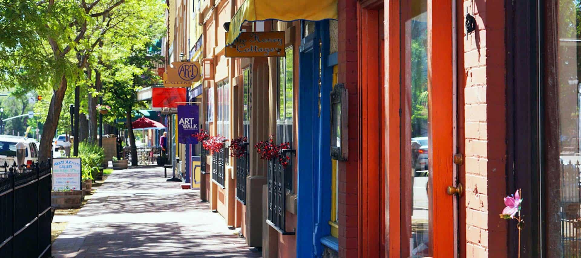 Main street sidewalk with retail stores, restaurants, and green trees