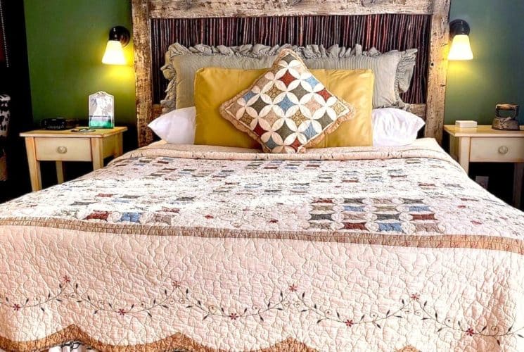 Bedroom with green walls, light colored carpeting, antique wooden headboard, multicolored bedding, and white wooden nightstands