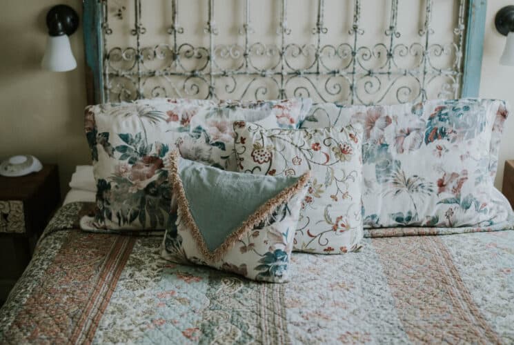 Bedroom with yellow walls, antique wood and white wrought iron headboard, multicolored bedding, and white wooden nightstands