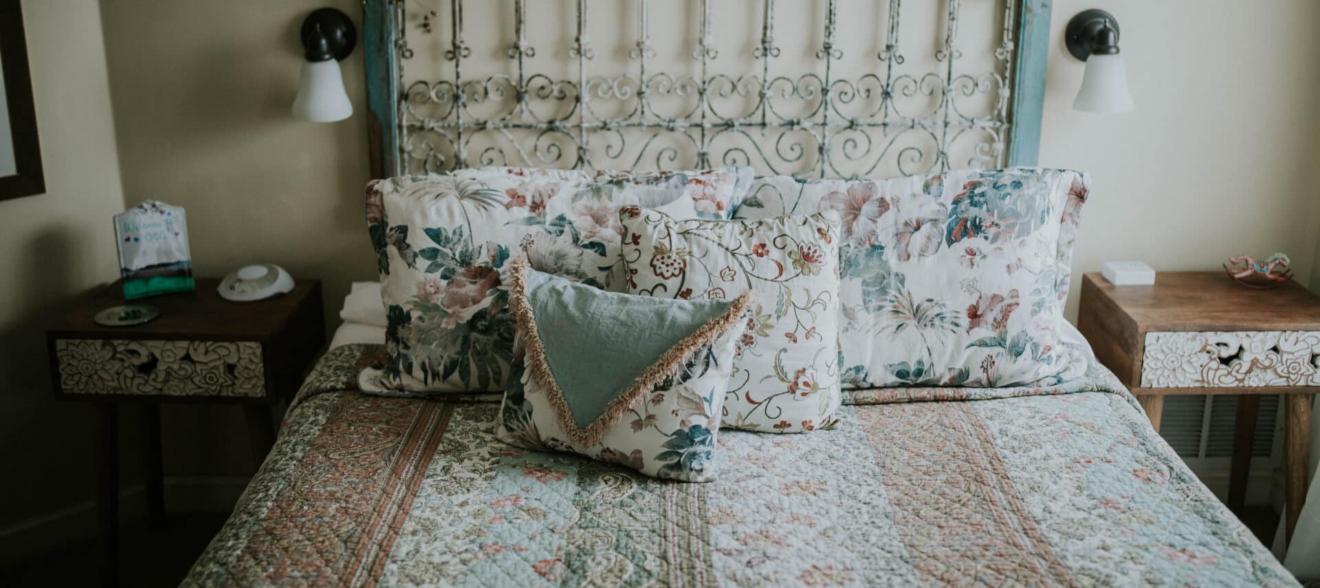 Bedroom with yellow walls, antique wood and white wrought iron headboard, multicolored bedding, and white wooden nightstands