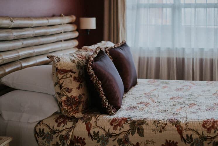 Bedroom with red walls, light colored carpeting, large bamboo rod headboard, multicolored bedding, and white wooden nightstands