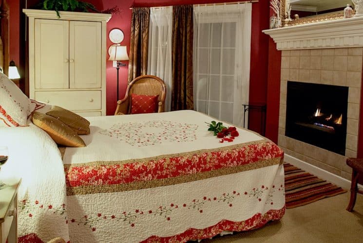 Bedroom with red walls, light colored carpeting, large wooden headboard, red and white bedding, white wooden nightstand and armoire, and fireplace