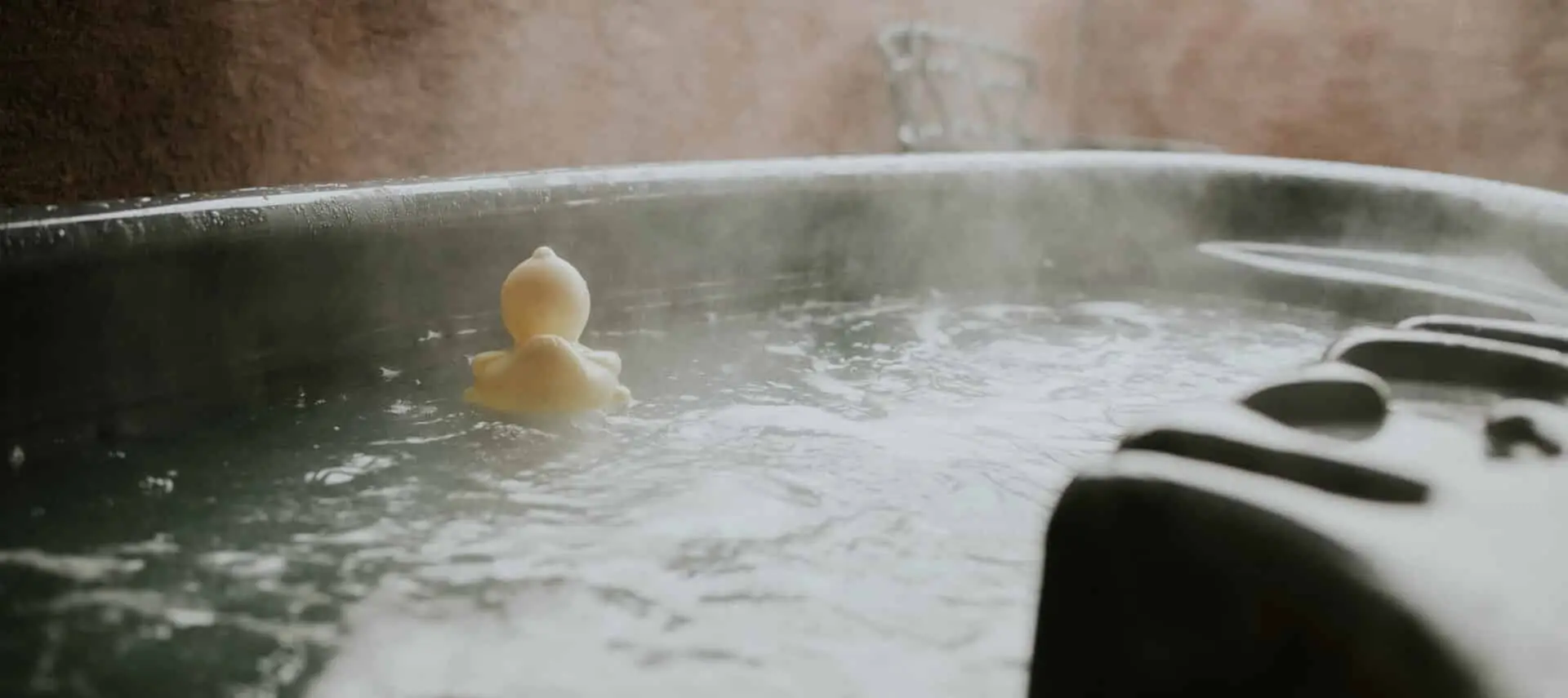 a small yellow rubber duck sits in a steaming hot tub