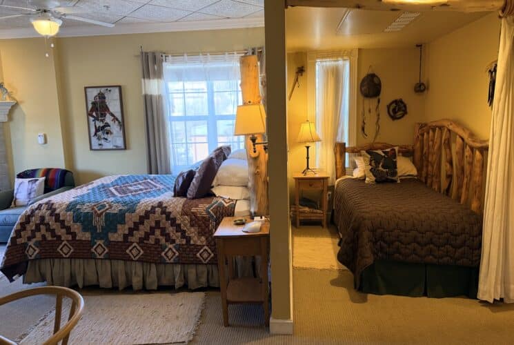 Split-bedroom room with a queen bed on the left featuring a Southwestern-style quilt and a rustic log-frame bed on the right, divided by a partial wall and warm lamps.