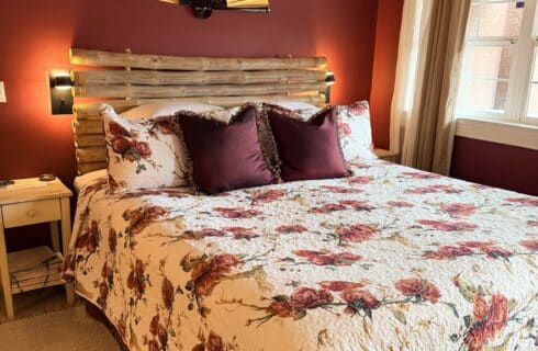Cozy bedroom with burgundy walls, a bamboo headboard, floral quilt, and plum throw pillows; bedside tables and soft window light.