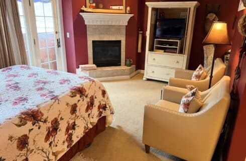 Cozy bedroom with a floral quilted bed, white fireplace, and burgundy walls across from a white TV cabinet