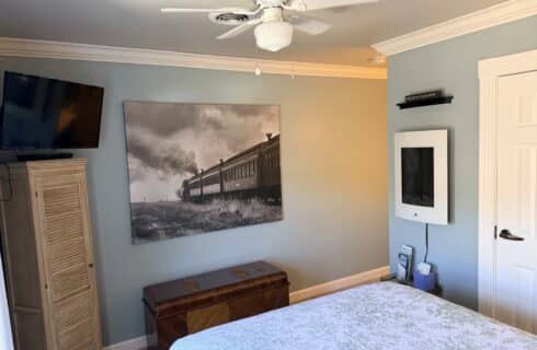 Bedroom with blue walls, ceiling fan, and a large black-and-white train photograph above a wooden chest at the foot of the bed